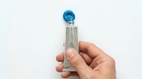Hand holding glass perfume bottle with blue cap against white background for cosmetic and fragrance product photography.
