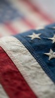Vintage worn American flag with weathered fabric texture showing patriotic red white and blue colors and embroidered stars in close-up detail.