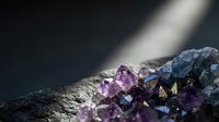 Purple and blue crystal formations with dramatic lighting on dark textured surface for luxury jewelry design and mineral collection displays.