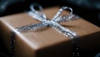 Elegant brown gift box wrapped with sparkling silver ribbon bow against dark background, creating magical holiday atmosphere with soft bokeh effect.