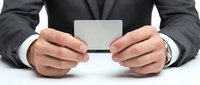 Businessman in dark suit holding blank white business card with both hands on white background for corporate branding.