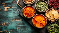 Colorful dried fruits and vegetables in wooden bowls on rustic turquoise background. Healthy snacks and ingredients for cooking arranged in composition.