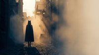 Mysterious silhouette walking through foggy cobblestone street at dawn with dramatic sunlight streaming between old buildings creating atmospheric urban scene.