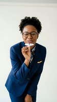 Smiling African American female pilot in navy uniform holding paper airplane on white background for aviation career and travel industry concepts.