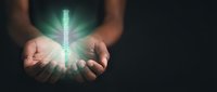 Hands holding glowing digital thermometer with bright light rays emanating from center against dark background for healthcare and medical technology concepts.