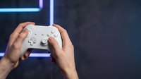 Gamer holding white wireless controller with neon blue light in dark gaming room environment for entertainment and esports content.