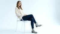 Young Caucasian woman in white sweater and jeans sitting on modern chair against white background, isolated for business and lifestyle concepts.