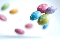 Colorful sugar-coated candy eggs floating in air against white background, soft focus effect creates dreamy atmosphere. Sweet treats captured in motion.