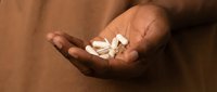 Close-up of open palm holding white medication pills and capsules against warm brown fabric background for healthcare and pharmaceutical concepts.