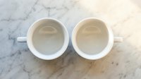 Two empty white ceramic coffee mugs on marble surface viewed from above for kitchen and cafe design projects.
