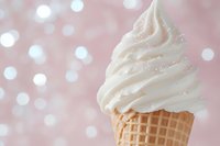 Vanilla soft serve ice cream cone with swirled white frosting against dreamy pink bokeh background for summer dessert and sweet treat concepts.