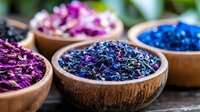 Colorful dried flower petals and herbs in wooden bowls arranged on rustic table, featuring vibrant blue, purple and pink organic botanical elements for spa and aromatherapy.