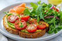 Healthy avocado toast with cherry tomatoes, microgreens and smoked salmon served on rustic bread. Fresh breakfast or lunch plate with green salad perfect for clean eating lifestyle.