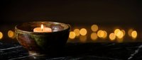 Handmade ceramic bowl with burning candle creating warm ambiance against soft bokeh lights background for relaxation and meditation practices.