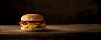 Juicy cheeseburger with melted cheese and bacon on rustic wooden table against dark background, dramatic lighting creates appetizing mood for food photography.