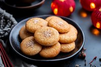 Fresh baked sugar cookies with sprinkled salt on black ceramic plate, festive holiday atmosphere with glowing red lights and spices in background.