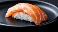 Fresh salmon nigiri sushi piece on black ceramic plate, featuring vibrant orange raw fish layered over pressed white rice, showcasing traditional Japanese cuisine.