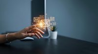 Businesswoman hand touching glowing email icons floating above desk, representing digital communication, messaging technology, and modern business correspondence solutions.