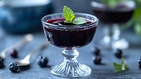 Fresh blackberry dessert mousse garnished with mint leaf in vintage glass on dark background, selective focus on creamy texture and berries.