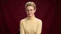 Professional blonde woman in yellow turtleneck sweater and glasses smiling confidently against burgundy background for business presentations.