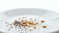 Assorted seeds and grains scattered on white ceramic plate including quinoa, chia, flax and legumes for healthy cooking and nutrition concepts.