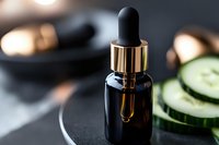Luxury skincare serum bottle with golden dropper and cucumber slices on dark surface for natural beauty treatment and cosmetic product photography.