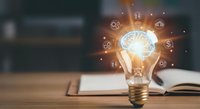 Light bulb with glowing brain and gear icons floating above open book on wooden desk representing innovation, creativity, learning and knowledge concepts.