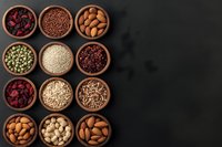 Variety of healthy nuts, seeds and dried berries in wooden bowls arranged in grid pattern on dark background with copy space. Top view of nutritious snacks.