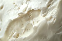 Creamy white texture with soft waves and bubbles creates abstract background pattern, macro photography of dairy product surface with delicate light and shadows.