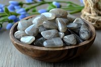 Polished moonstone crystals in wooden bowl with blue spring flowers, natural healing stones for meditation and spiritual practices on rustic surface.