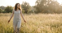 Young woman with curly hair walking through golden wheat field at sunset wearing white dress enjoying peaceful moment in nature countryside landscape.