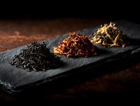 Assortment of loose leaf tea varieties on black slate board against dark background, showcasing different colors and textures for gourmet tea service.