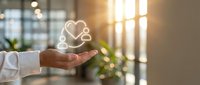 Hand holding glowing heart and medical cross symbol representing healthcare compassion and wellness in modern office environment with warm lighting.