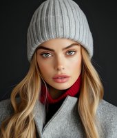 Young Caucasian woman with blonde hair wearing gray knit beanie, red turtleneck and wool coat against dark background. Close up winter fashion portrait.