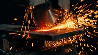 Industrial worker grinding metal with angle grinder creating dramatic sparks in workshop manufacturing environment for metalworking and fabrication projects.