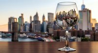 Wine glass with city skyline reflection at sunset creating artistic urban dining concept for restaurant marketing and hospitality industry promotional materials.