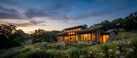 Modern luxury home with warm lighting at sunset surrounded by native landscaping and rolling hills creating peaceful residential atmosphere.