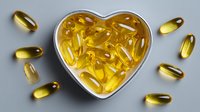 Golden omega-3 fish oil capsules in heart-shaped container, symbolizing cardiovascular health benefits and nutritional supplements.