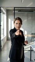 Confident middle-aged Caucasian businesswoman in black suit pointing forward in modern glass office, leadership and determination concept for corporate training.