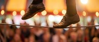 Person walking on tightrope at sunset with warm bokeh lights in background. Balance, courage and determination concept for business success.