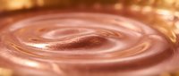 Young woman with medium skin tone applying rose gold liquid cosmetic product, swirling motion creating concentric circles in metallic makeup or skincare serum for beauty and wellness applications.