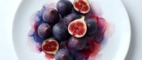 Fresh ripe figs with purple skin and red flesh arranged on white plate with watercolor splash effect for culinary and food photography projects.