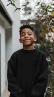 Young African American boy with bright smile wearing black sweatshirt outdoors, natural lighting and soft bokeh background creates warm authentic mood.