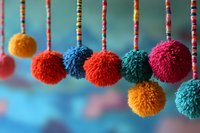 Colorful yarn pompoms hanging on striped strings create festive party decoration against soft blue background for celebrations and craft projects.