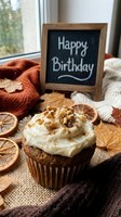 Autumn carrot cupcake with cream cheese frosting and walnuts beside a Happy Birthday chalkboard sign, dried oranges, and fall leaves.