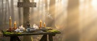 Mystical altar setup with burning candles, crystals, dried herbs and wooden cross creating atmospheric spiritual ritual scene with warm golden light rays.