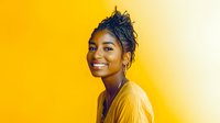 Young African American woman with natural hair and bright smile wearing yellow sweater against vibrant yellow background, radiating joy and confidence in studio portrait.