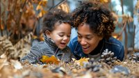 African American mother and young son share joyful moment playing in fallen autumn leaves outdoors, expressing genuine happiness and family bonding in nature.