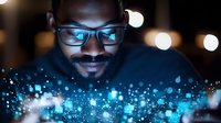 African American man in glasses illuminated by blue digital screen glow at night, with bokeh light effects creating magical technology atmosphere.