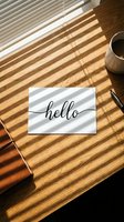Hello greeting card with cursive script on wooden desk with sunlight shadow stripes, coffee cup, pen, and leather notebook for workspace concepts.